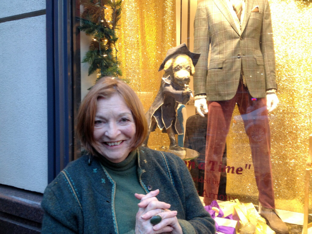 Elaine Badgley Arnoux posing with her art in the window of Wilkes Bashford